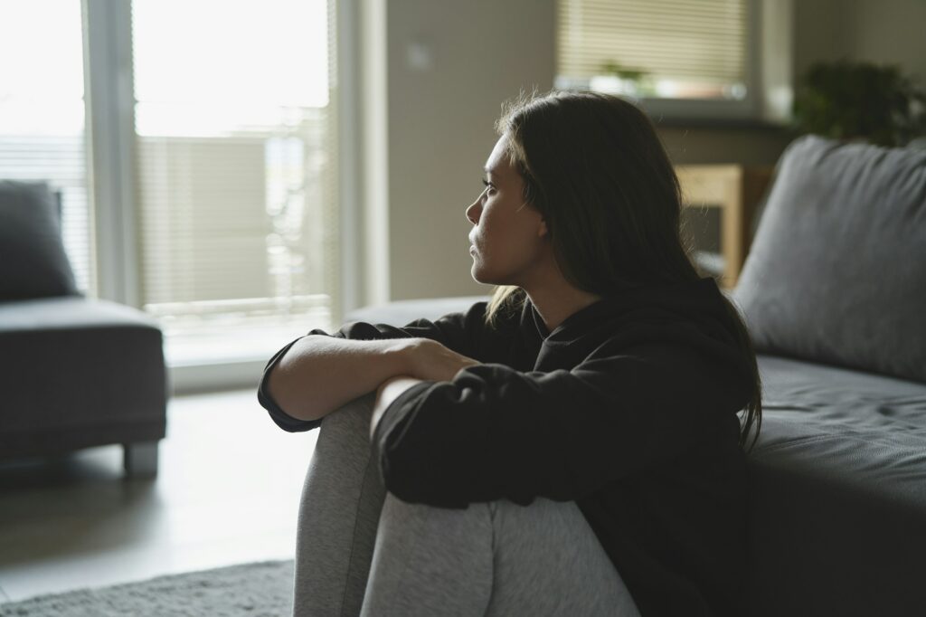 Caucasian sad woman sitting at the floor and looking throw window at home