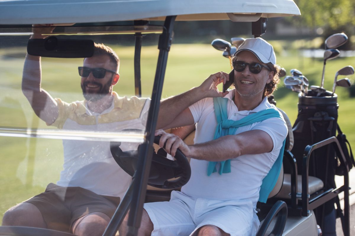 Handsome men are smiling while driving a golf cart and searching for a golf hole